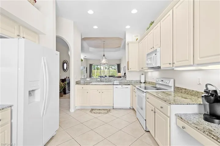 Kitchen with a tray ceiling, sink, white appliances, light tile floors, and pendant lighting