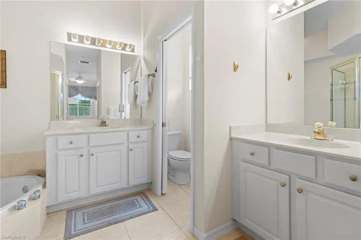 Bathroom featuring tiled bath, tile flooring, toilet, and large vanity