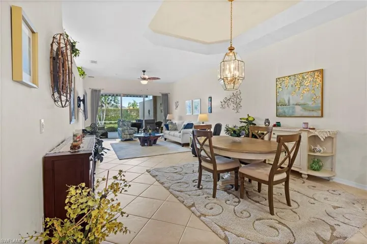 Dining space with a raised ceiling, ceiling fan with notable chandelier, and light tile floors