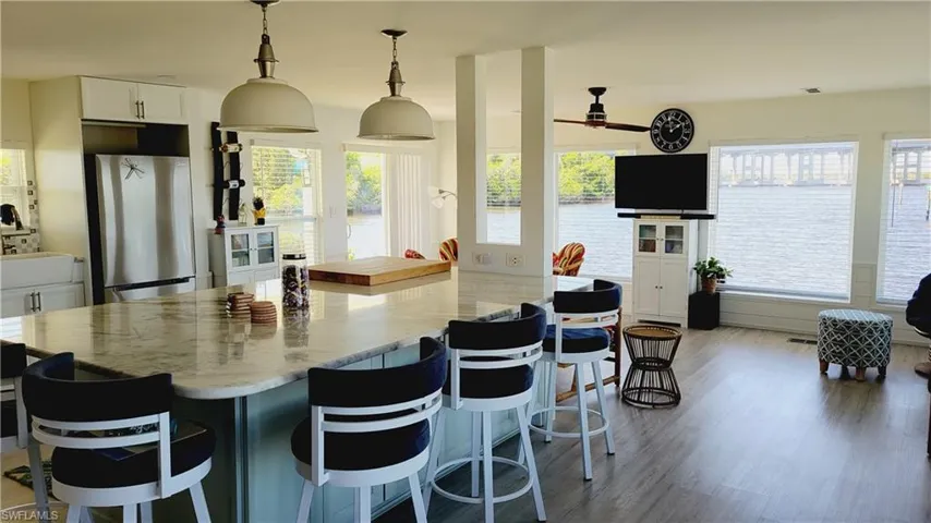 Kitchen featuring Large Marble Island with seating, white cabinets, vinyl planking finished floors, freestanding refrigerator, and pendant lighting