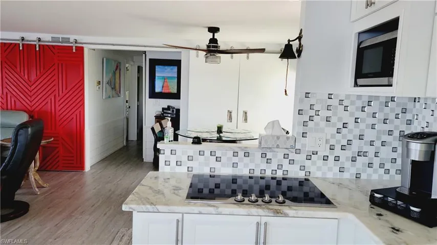 Kitchen with white cabinets, stainless steel microwave, marble counters, beautiful backsplash and black electric cooktop.