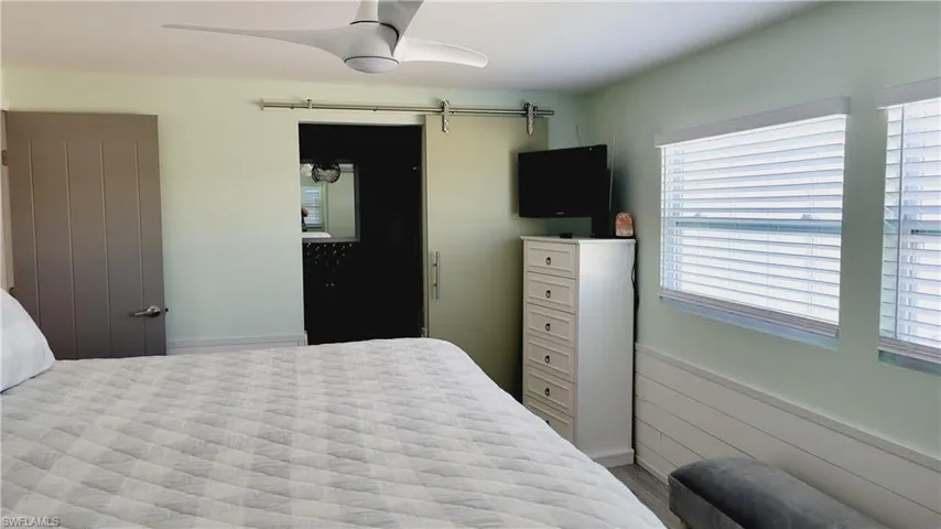 Master bedroom featuring a wainscoted wall, a barn door, and ceiling fan looking towards ensuite.
