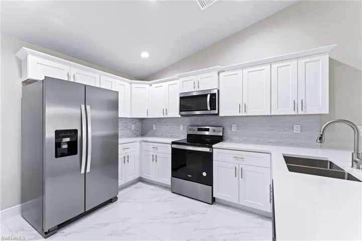 Kitchen featuring lofted ceiling, sink, appliances with stainless steel finishes, tasteful backsplash, and white cabinets