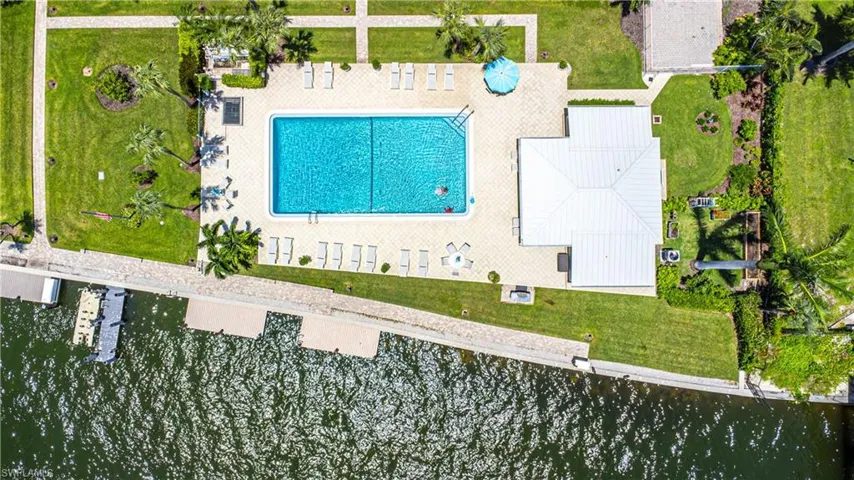 Community pool area featuring a rectangular pool with steps, surrounded by a paver deck with lounge seating