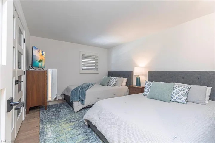Spacious Guest  room with light wood-finish flooring, white walls, and a window with plantation shutters