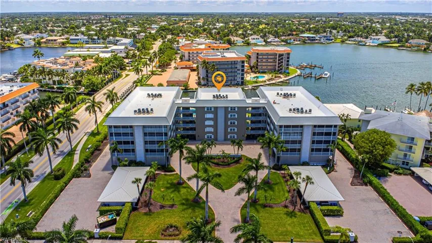 Expansive waterfront property featuring a multi-story residential building with balconies, multiple carports, and manicured landscaping