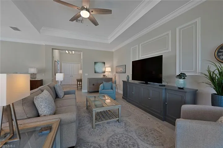 Living room with a tray ceiling, custom crown moldings, ceiling fan, and