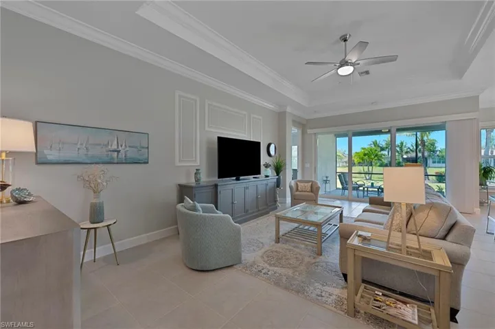 Living room featuring a tray ceiling, custom crown moldings, porcelain tile  floors, and ceiling fan