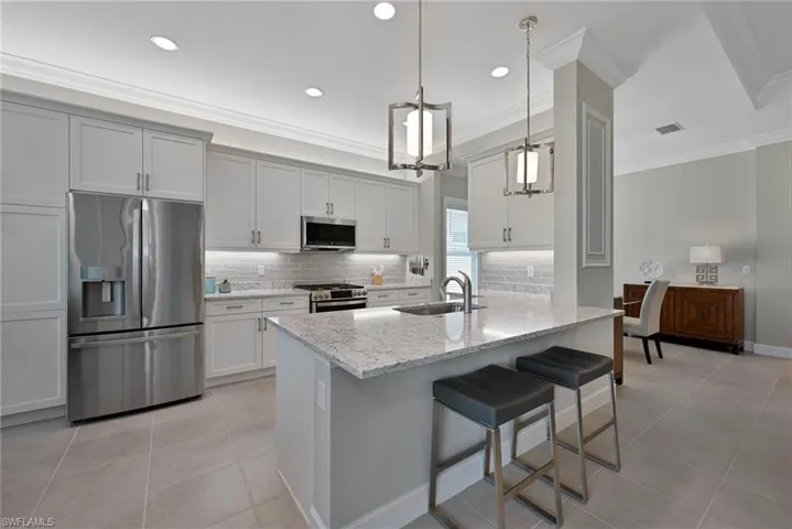 Kitchen with stainless steel appliances, tasteful backsplash, custom crown moldings, a kitchen bar, and light stone countertops