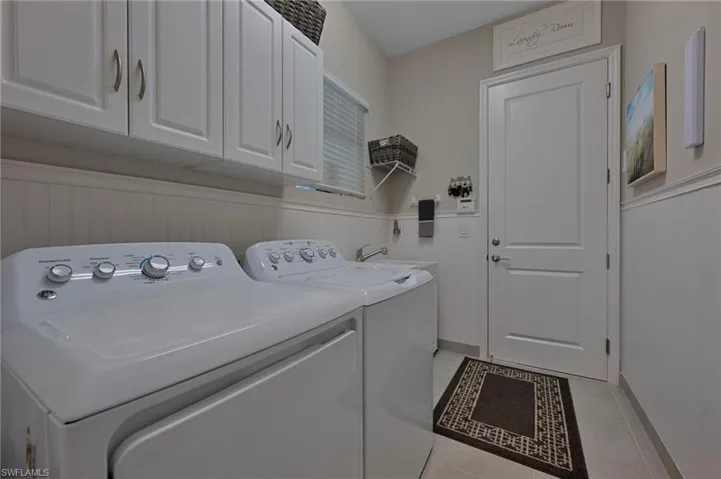 Laundry room with washing machine and dryer, cabinet space, light tile floors, and a wainscoted wall, sink