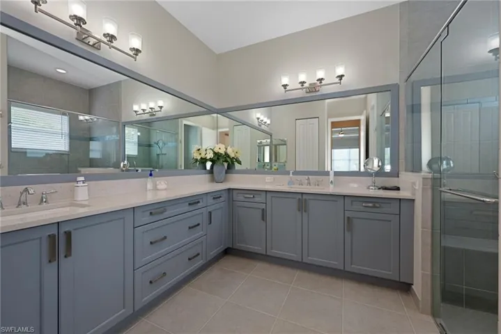 Full bath with natural light, double vanity, a stall shower, and porcelain tile flooring, framed mirrors