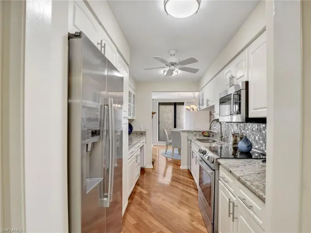 Kitchen featuring stainless steel appliances, white cabinetry, ceiling fan, decorative backsplash, and light wood finished floors