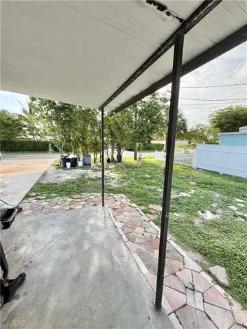 Covered patio featuring a concrete slab floor, decorative paver walkway, white vinyl fence, and mature trees
