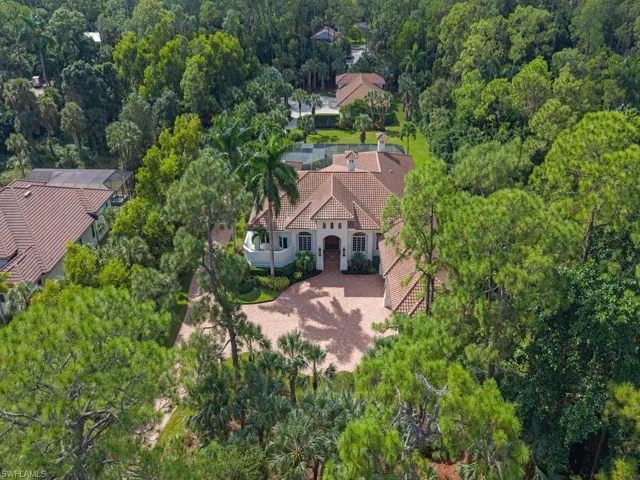 Mediterranean-style architecture with a tile roof, a circular paver driveway, lush landscaping.Visible behind the home a free standing building with three (3) additional garages and a half bath.