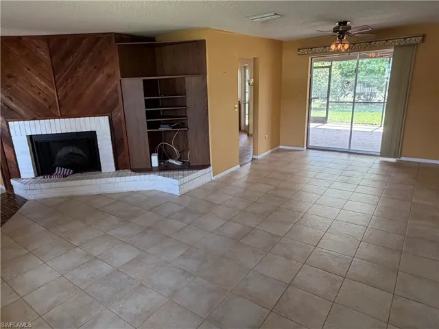 Unfurnished living room with a textured ceiling, light tile patterned floors, ceiling fan, and a fireplace