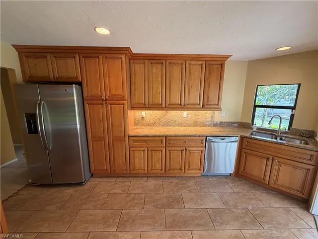 Kitchen with stainless steel appliances, light stone countertops, wood finish cabinetry, recessed lighting, and light tile patterned floors