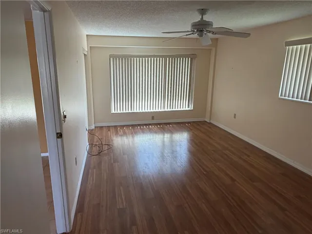 Empty room with a textured ceiling, a ceiling fan, and dark wood finished floors