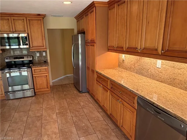 Kitchen with stainless steel appliances, wood finish cabinetry, light stone counters, and backsplash