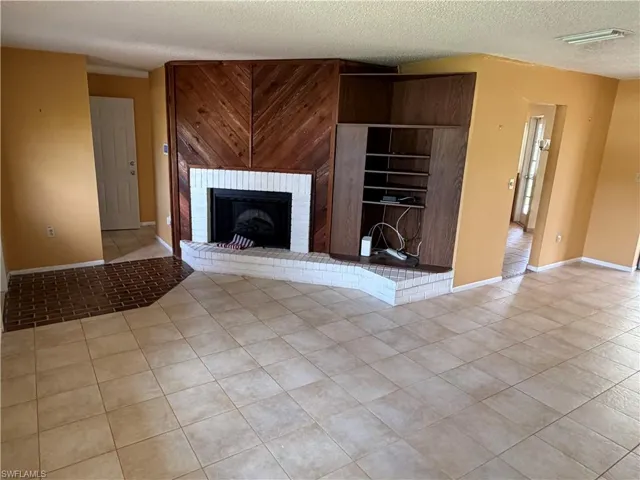 Unfurnished living room with light tile patterned flooring, a textured ceiling, and a brick fireplace