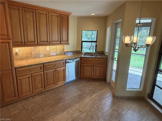 Kitchen featuring light stone countertops, dishwasher, wood finish cabinets, and suspended lighting