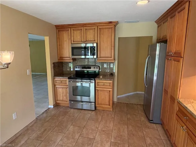 Kitchen with stainless steel appliances, dark stone countertops, wood finish cabinets, and backsplash