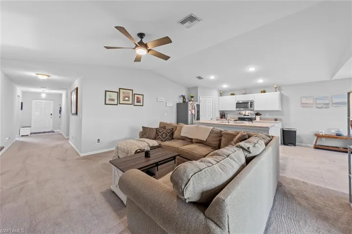 Carpeted living room with lofted ceiling, ceiling fan, and a baseboard heating unit