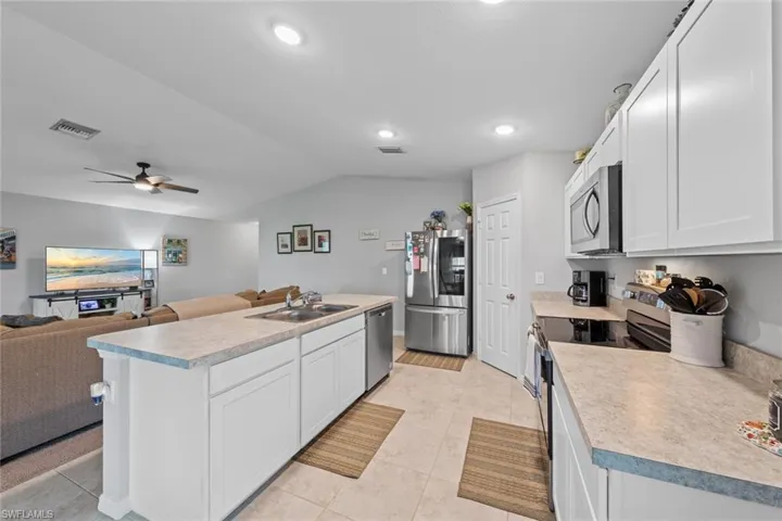 Kitchen featuring white cabinetry, stainless steel appliances, an island with sink, sink, and ceiling fan
