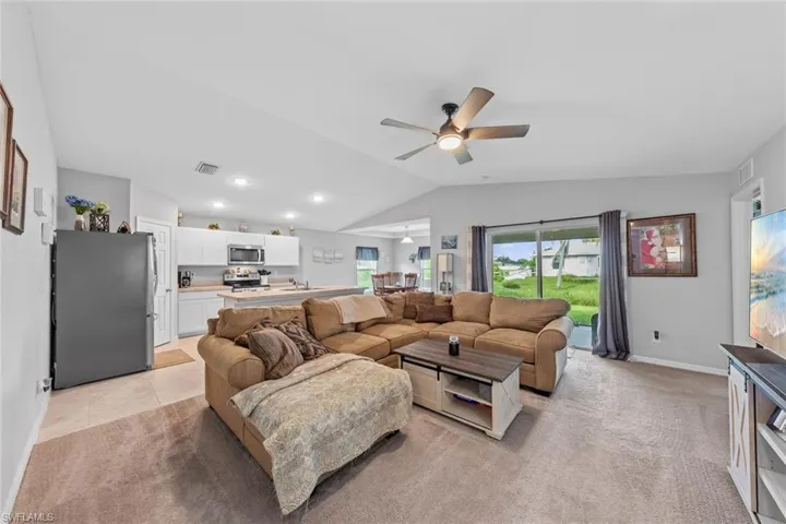 Living room with lofted ceiling, ceiling fan, light colored carpet, and sink