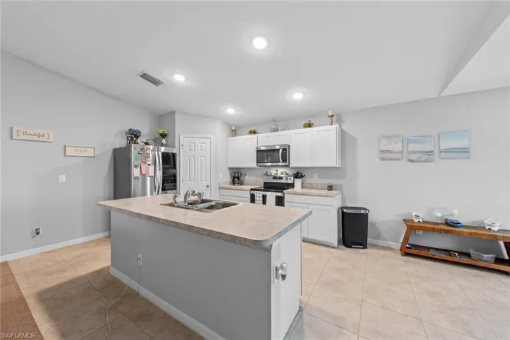 Kitchen with white cabinetry, light tile patterned floors, an island with sink, sink, and appliances with stainless steel finishes