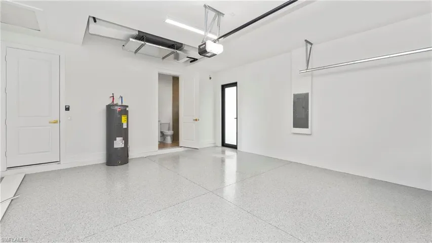 Garage with electric water heater, electric panel, and a garage door opener