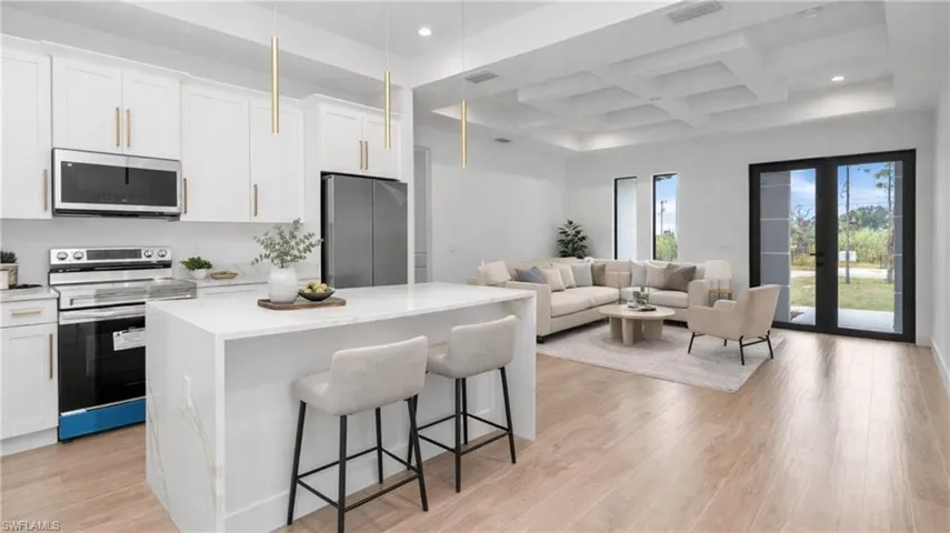 Virtually Staged Kitchen with stainless steel appliances, coffered ceiling, a kitchen breakfast bar, a kitchen island, and white cabinetry