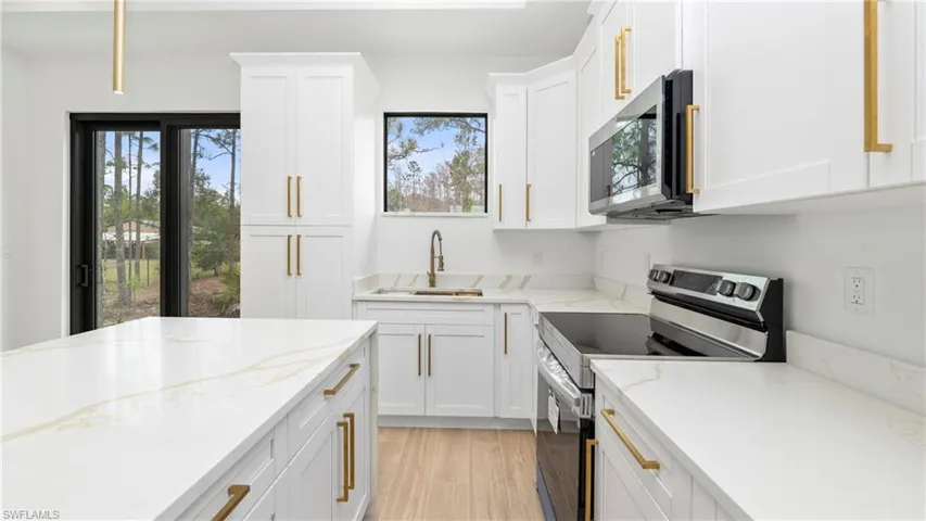 Kitchen featuring stainless steel appliances, light stone countertops, healthy amount of natural light, and white cabinets