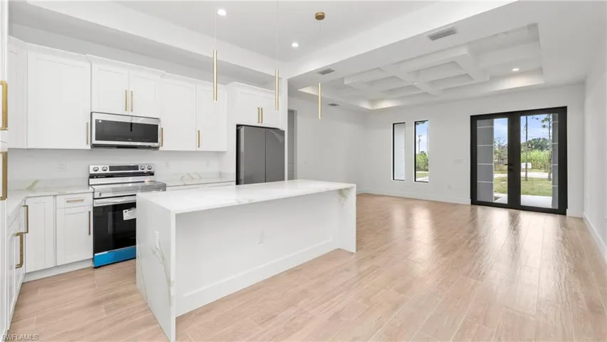 Kitchen featuring coffered ceiling, stainless steel appliances, a kitchen island, pendant lighting, and light stone countertops