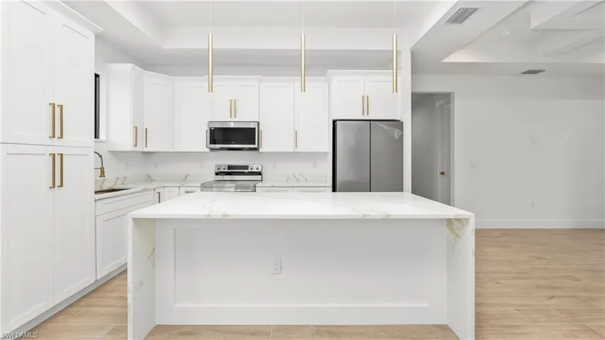 Kitchen featuring light stone counters, a tray ceiling, stainless steel appliances, and a kitchen island