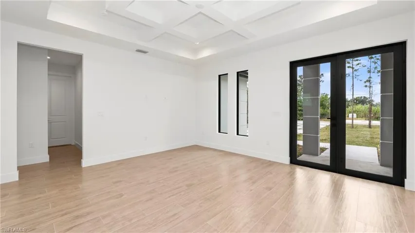 Spare room featuring coffered ceiling, light wood finished floors, french doors, and beamed ceiling