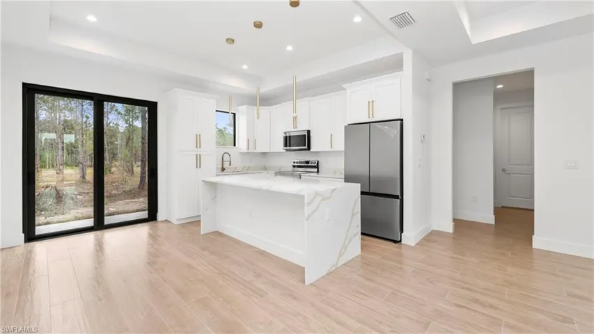 Kitchen with stainless steel appliances, light stone countertops, white cabinetry, hanging light fixtures, and a raised ceiling
