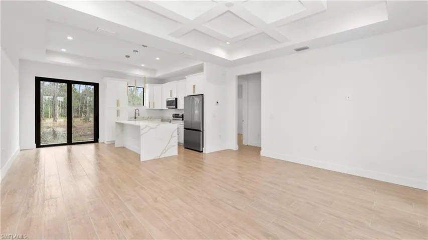 Kitchen with open floor plan, coffered ceiling, a raised ceiling, stainless steel appliances, and white cabinets