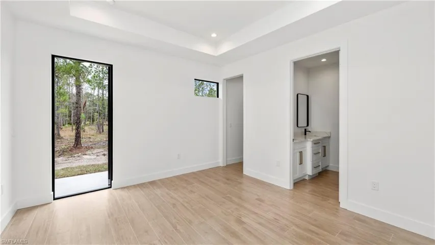 Unfurnished bedroom with light wood-style flooring, connected bathroom, access to exterior, a raised ceiling, and recessed lighting