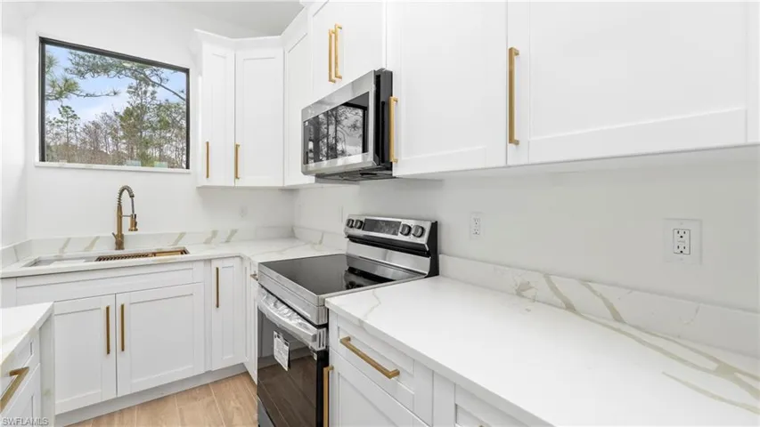 Kitchen featuring stainless steel appliances, light stone counters, white cabinetry, and light wood-style floors