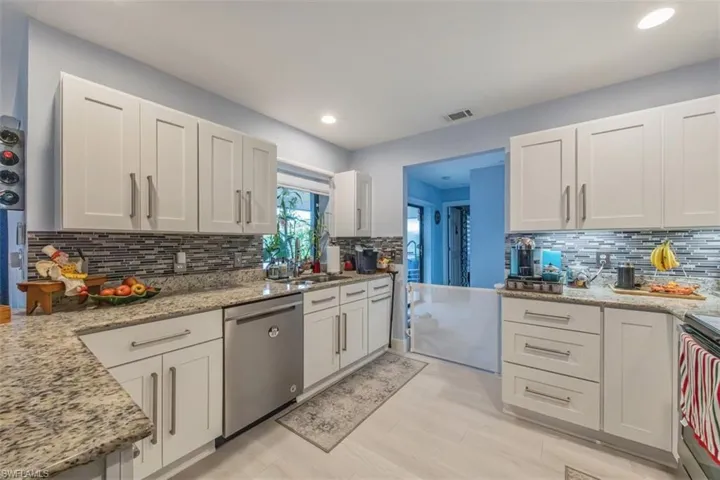 Kitchen featuring white cabinetry, stainless steel appliances, light stone countertops, decorative backsplash, and recessed lighting