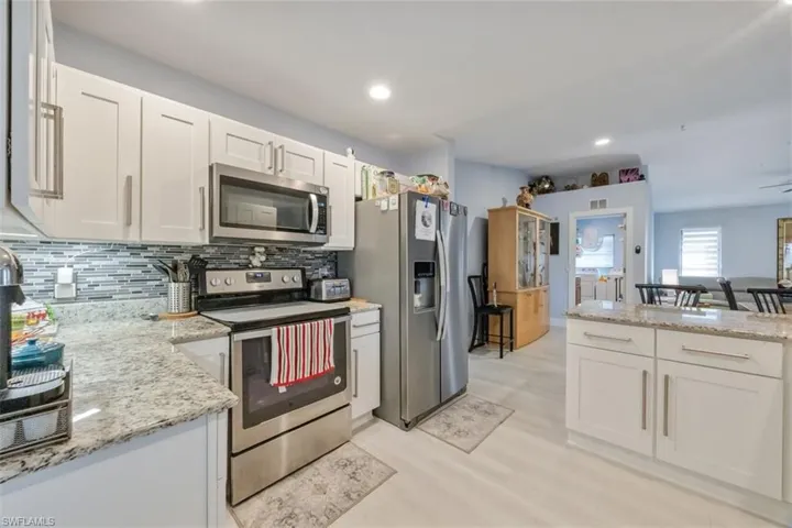 Kitchen with stainless steel appliances, white cabinetry, light stone countertops, decorative backsplash, and recessed lighting