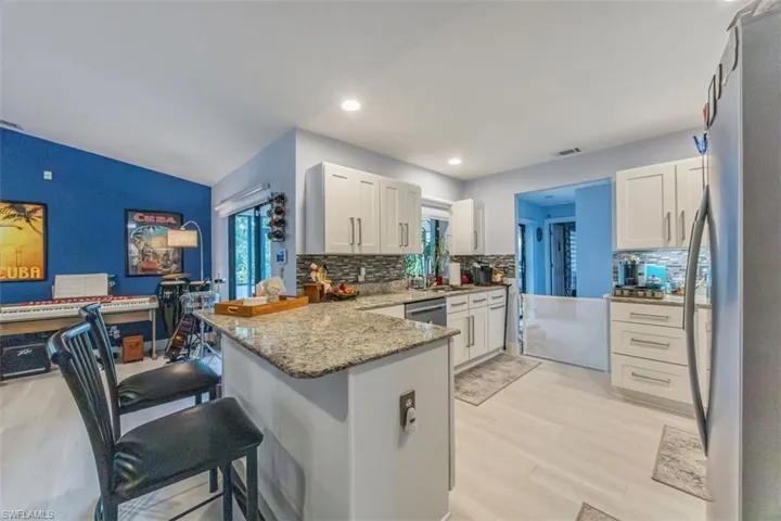 Kitchen with appliances with stainless steel finishes, light stone countertops, a breakfast bar area, light wood-type flooring, and white cabinetry