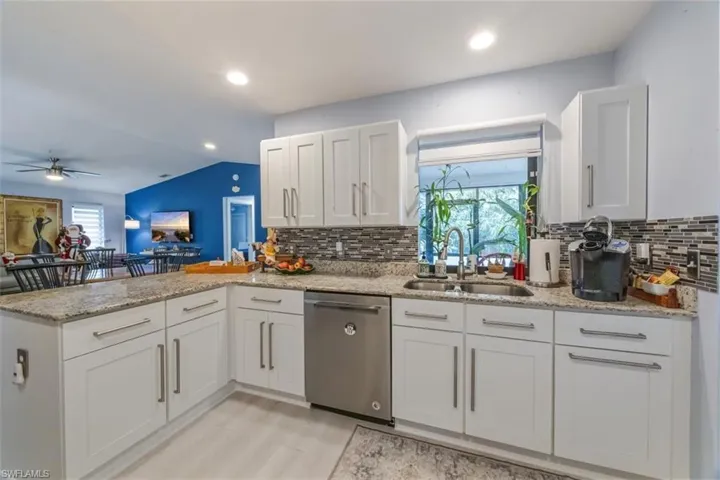 Kitchen with white cabinetry, dishwasher, light stone counters, a peninsula, and vaulted ceiling