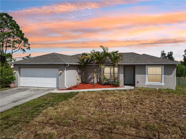 Ranch-style house featuring driveway, stucco siding, an attached garage, a front lawn, and a shingled roof