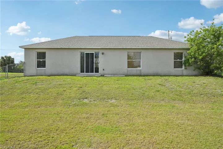 Back of house featuring stucco siding, fence, and a yard