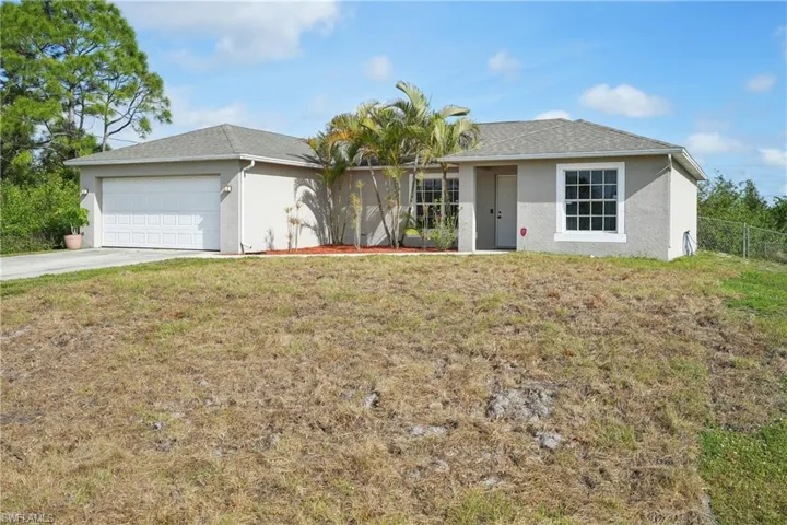 Ranch-style house featuring a front lawn, driveway, stucco siding, and an attached garage