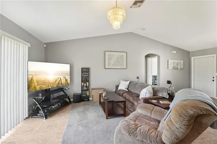Living room featuring lofted ceiling, an inviting chandelier, light tile patterned floors, arched walkways, and visible vents
