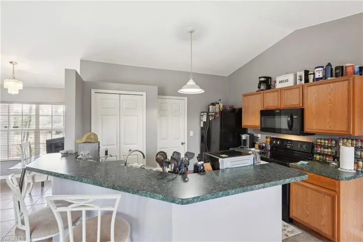 Kitchen with a kitchen bar, dark countertops, lofted ceiling, black appliances, and light tile patterned floors