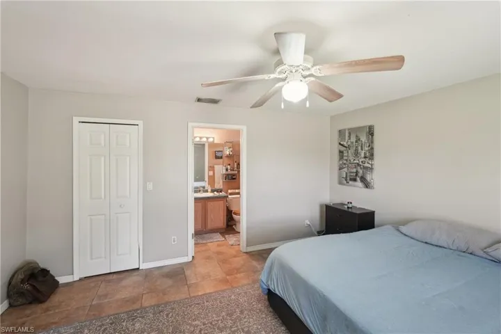 Bedroom featuring ensuite bathroom, a closet, visible vents, baseboards, and ceiling fan