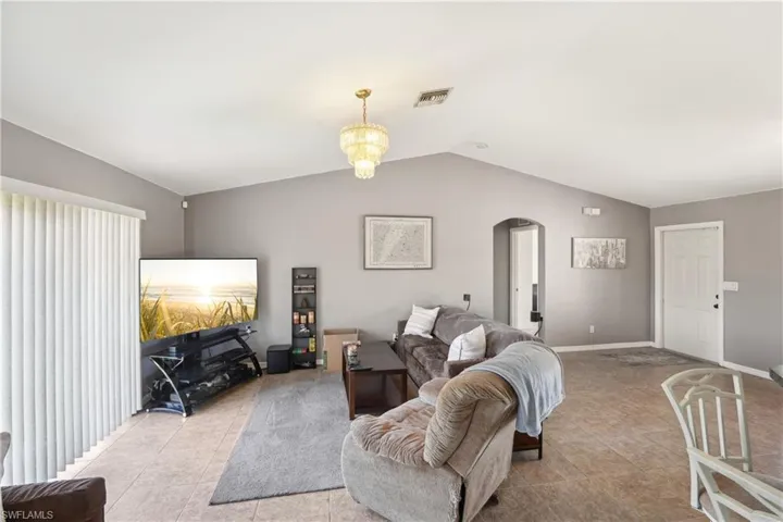 Living room featuring arched walkways, baseboards, vaulted ceiling, and visible vents